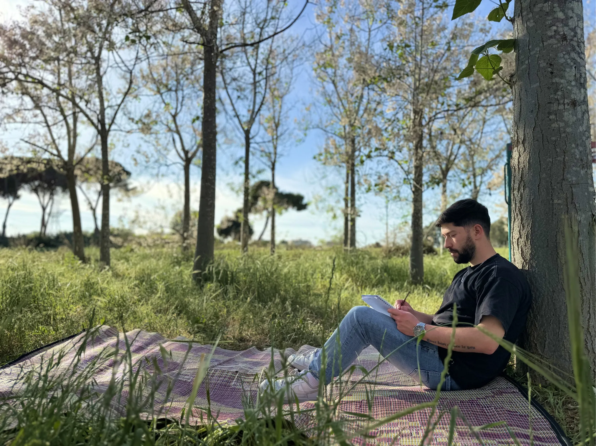 Sefi sitting against a tree, sketching in a notebook